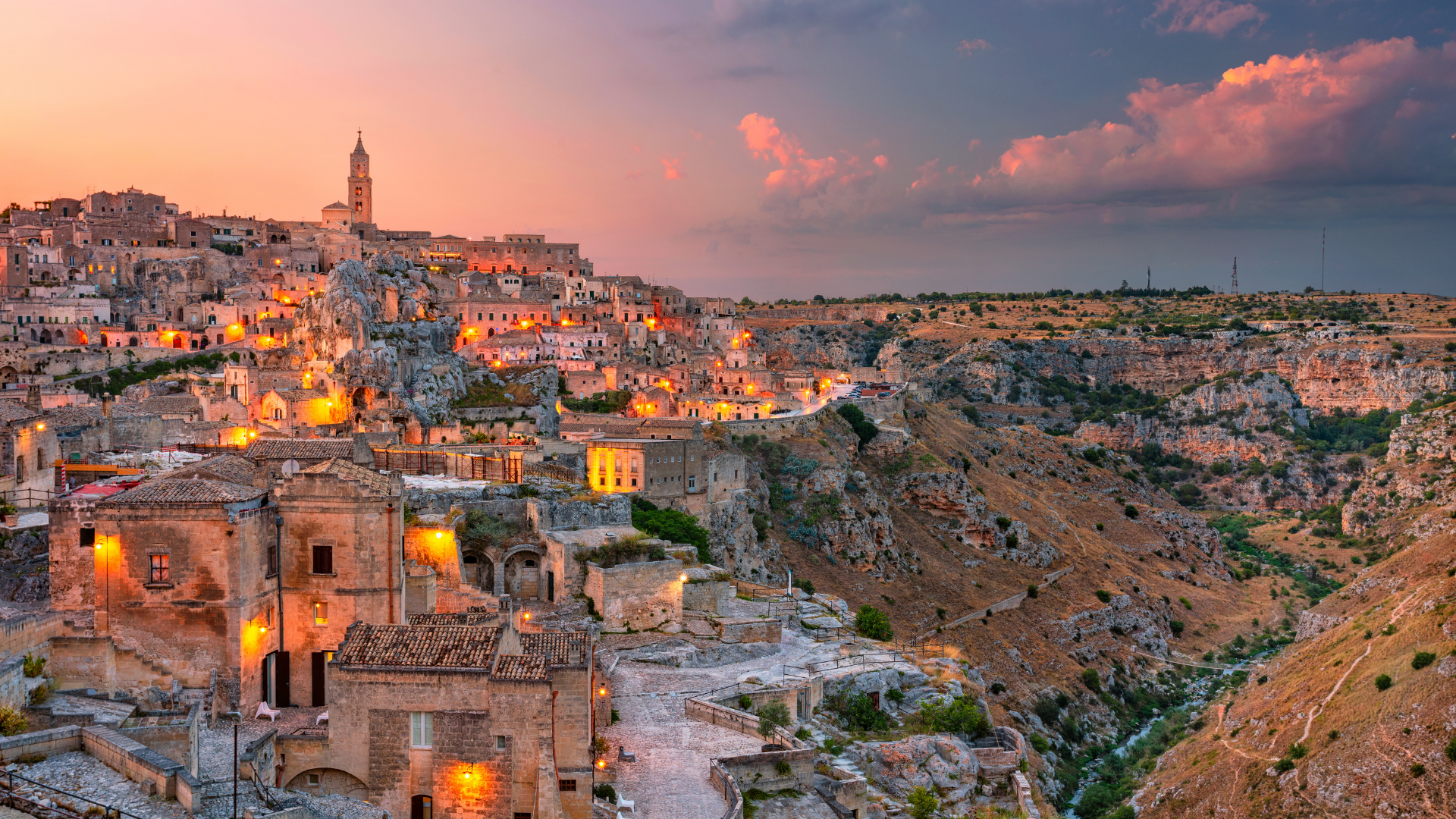 I Sassi di Matera illuminati al tramonto sopra la gravina, con il campanile della Cattedrale