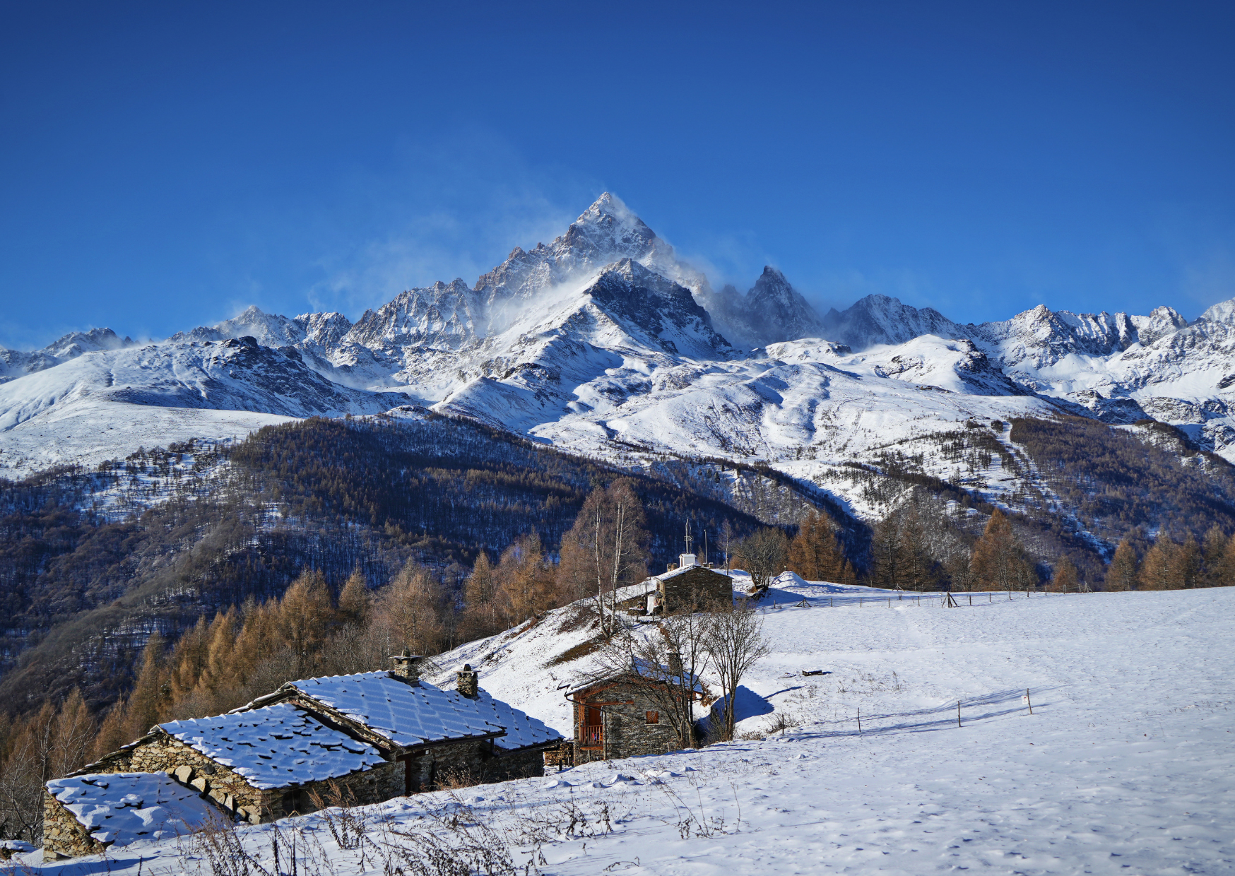 Cima piramidale innevata sopra baite in pietra con tetti in lose, sul versante che guarda Ostana