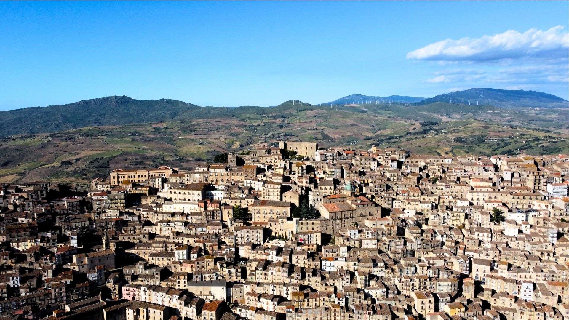 Veduta aerea di Gangi sul crinale, con le colline delle Madonie e un parco eolico sullo sfondo