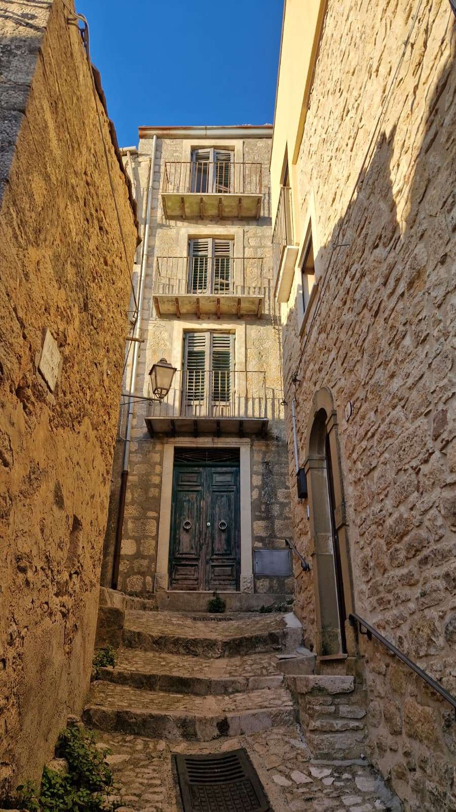 Vicolo a gradini di Gangi con il portone ligneo verde di un palazzo in pietra e il lampione in ferro battuto